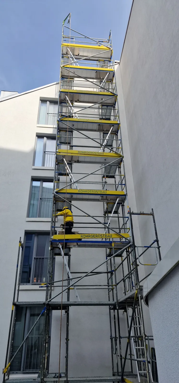 Hoher Fassaden- und Treppenturm aus Stahlrohrgerüst gegen blauen Himmel – Gerüstbau Hamburg